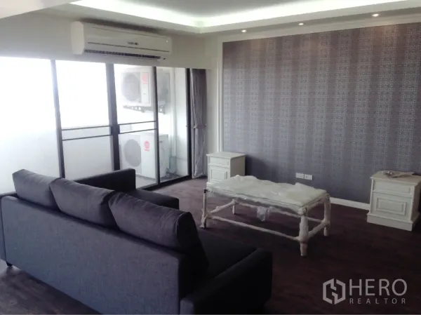 Condominium for rent or sale in Chatuchak, Bangkok - Living room with gray sofa, sliding doors to the balcony, air conditioner, and textured feature wall.