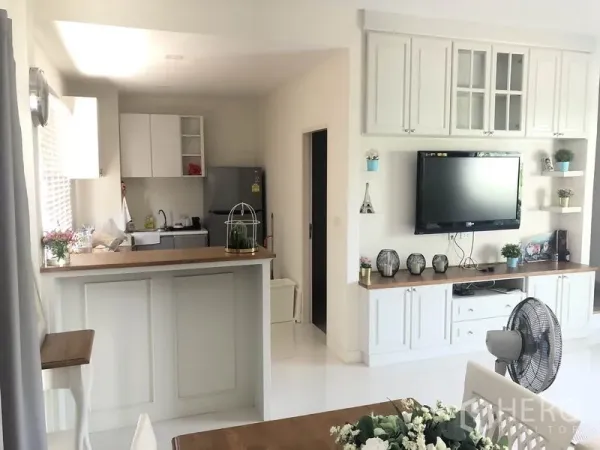 Townhouse for rent or sale in Saphan Sung, Bangkok - Bright open-plan kitchen with white cabinetry, breakfast bar, and built-in TV wall in the living area.