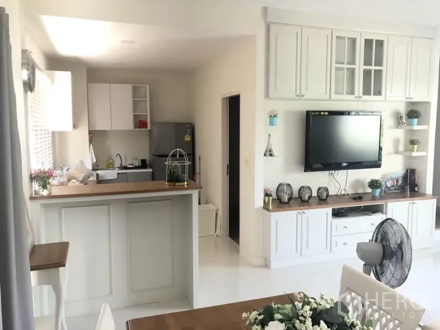 Townhouse for rent or sale in Saphan Sung, Bangkok - Bright open-plan kitchen with white cabinetry, breakfast bar, and built-in TV wall in the living area.