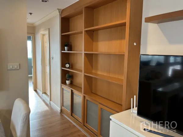 Condominium for rent or sale in Watthana, Bangkok - Built-in wooden shelving unit beside TV cabinet along the living area wall.