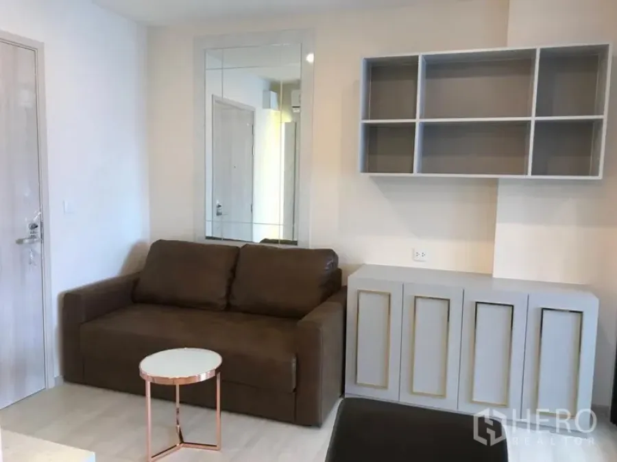 Condominium for rent in Huai Khwang, Bangkok - Bright living area with a brown sofa, wall mirror, built-in shelves and cabinet.