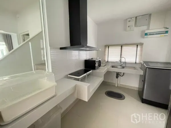 Detached House for rent or sale in Bang Phli, Samut Prakan - Compact kitchen with cooktop, hood, sink and appliances by a window.