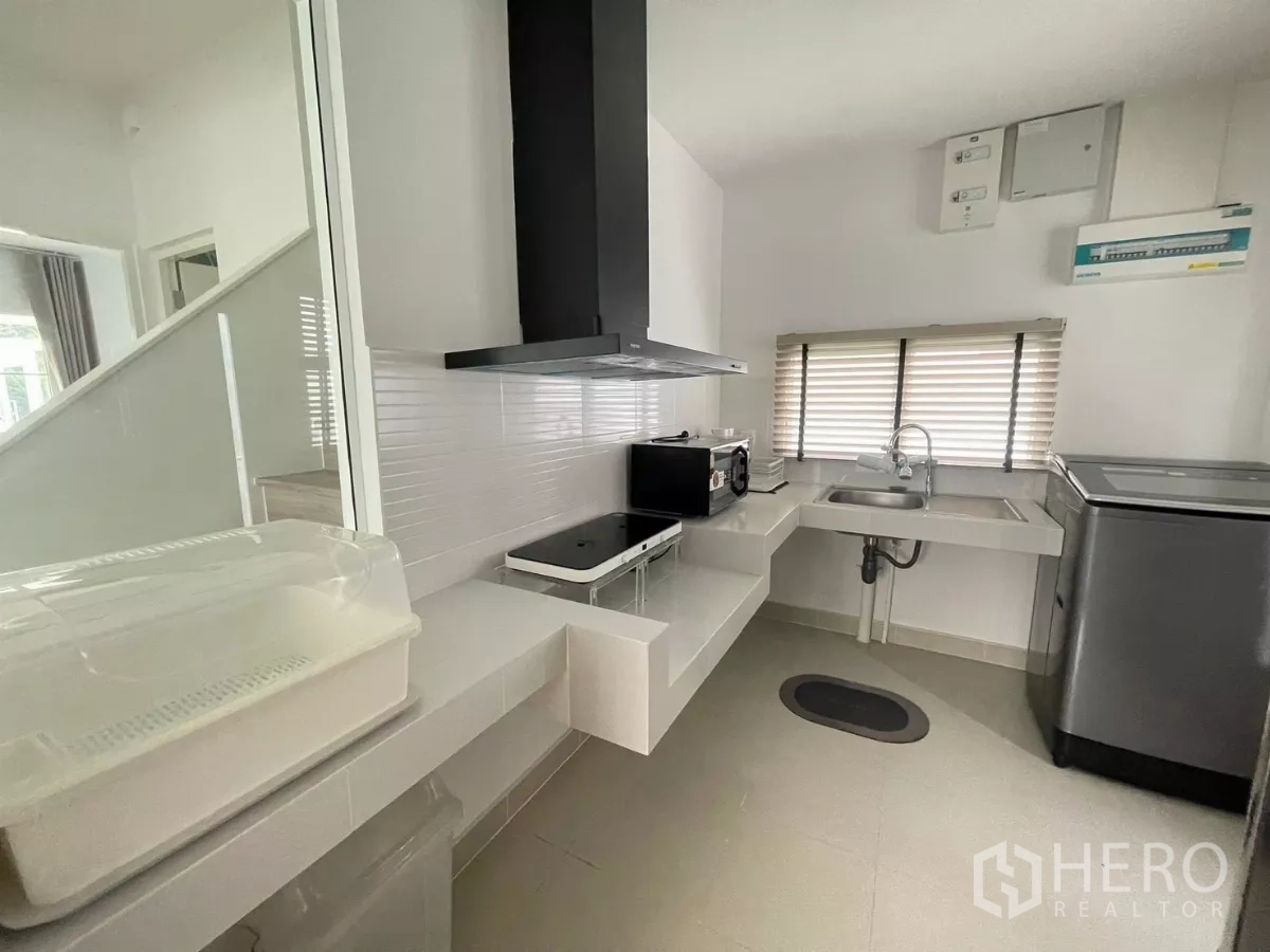 Detached House for rent or sale in Bang Phli, Samut Prakan - Compact kitchen with cooktop, hood, sink and appliances by a window.