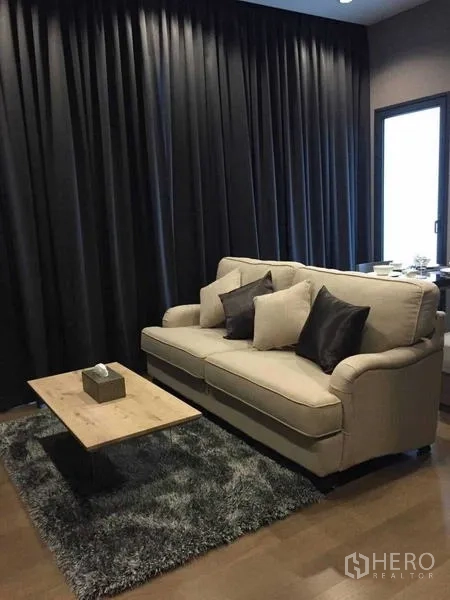 公寓 出租在Bang Rak, Bangkok - 起居区配米色沙发、木质茶几与深色窗帘，木地板。