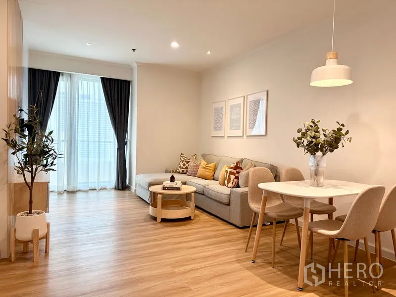 คอนโด ให้เช่าในKhlong San, Bangkok - ห้องนั่งเล่นและรับประทานอาหารสว่าง โซฟาเข้ามุม โต๊ะกาแฟทรงกลม พื้นไม้ และม่านบานประตูระเบียง