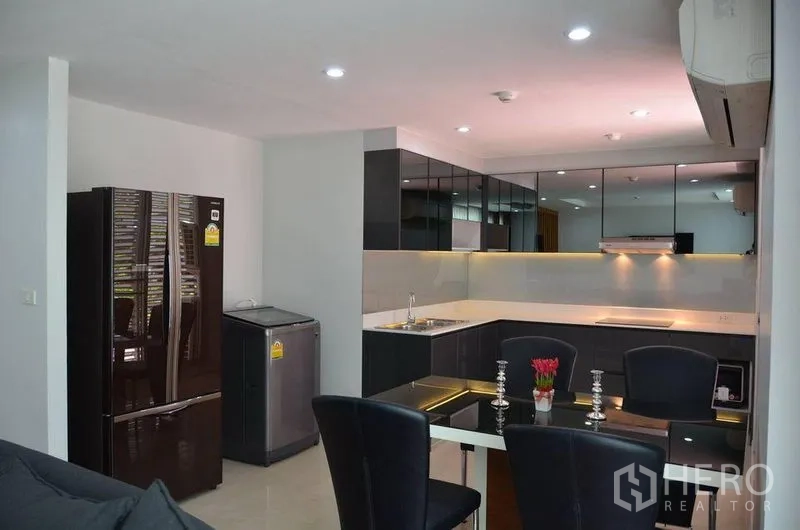 Condominium for rent in Watthana, Bangkok - Open-plan living and dining area with dark sofa set, glass coffee table, wood-slat feature partition and recessed lighting.