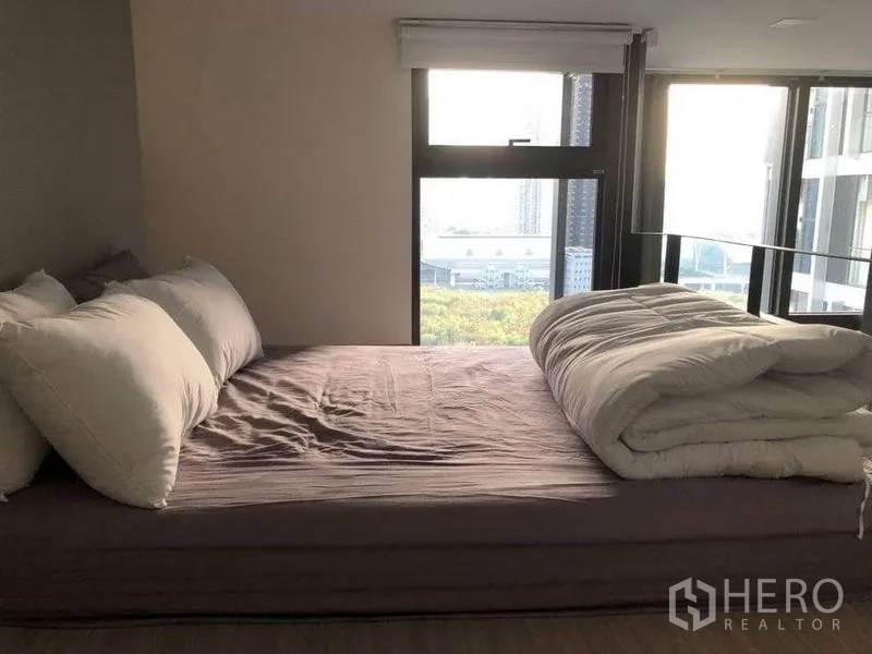 Condominium for sale in Ratchathewi, Bangkok - Cozy bedroom with large windows and city view, sunlight over a queen bed.