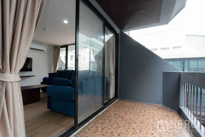 Apartment for rent in Khlong Toei, Bangkok - Covered balcony with tiled floor and sliding glass doors opening to the living room.