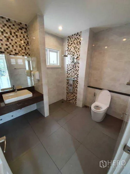 联排别墅 出租在Bang Na, Bangkok - 卫浴带马赛克点缀墙、雨淋花洒、镜柜与灰色地砖。