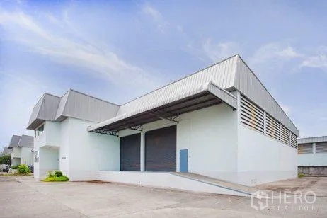 Warehouse for rent in Bang Phli, Samut Prakan - Modern warehouse exterior with dock-high loading bays, ramp access, and a wide concrete yard.