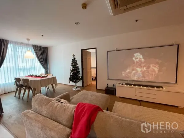 คอนโด ให้เช่าหรือขายในWatthana, Bangkok - มุมนั่งเล่นมีโซฟารับแขกหันเข้าหาหน้าจอโปรเจคเตอร์ ข้างหน้าต่างผ้าม่านยาวและมุมทานอาหาร