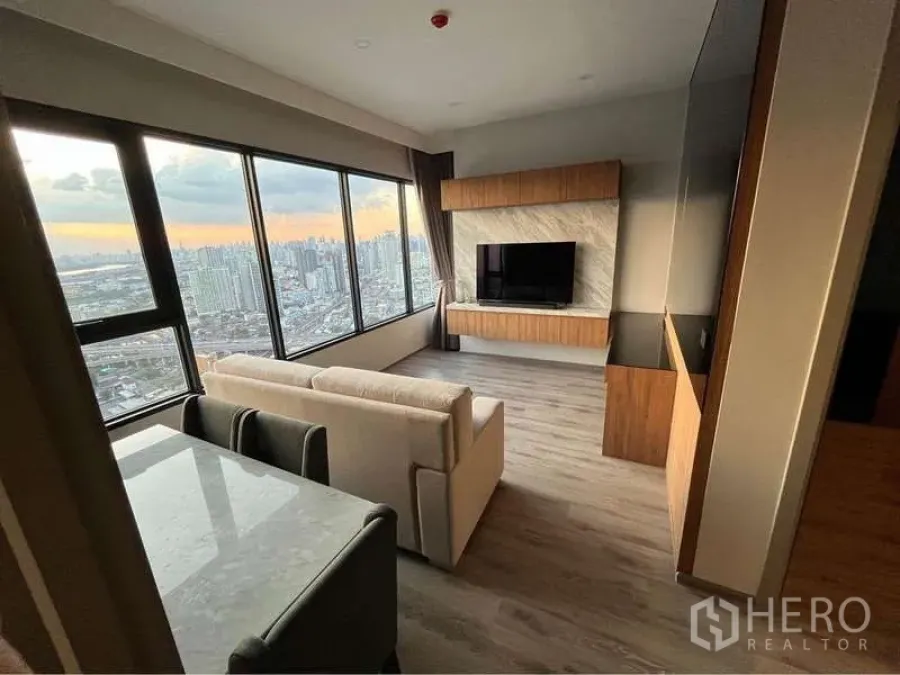 公寓 出租在Watthana, Bangkok - 黄昏时的客餐一体空间，环窗视野、沙发、石质餐桌与时尚电视背景墙。