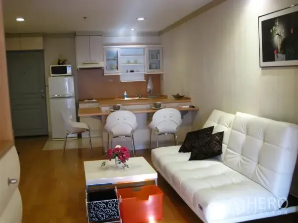 คอนโด ให้เช่าในKhlong Toei, Bangkok - พื้นที่นั่งเล่นแบบเปิดพร้อมโซฟาสีขาว พื้นไม้ และครัวขนาดกะทัดรัดพร้อมเคาน์เตอร์บาร์