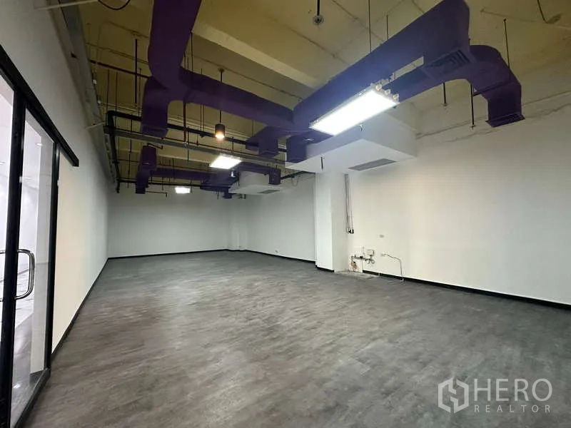 办公空间 出租 - 宽敞办公室内景，带玻璃入口门，工业风天花与明亮灯光，靠近BTS奇隆站。