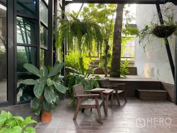 Office Space for rent in Bang Kapi, Bangkok - Shaded garden patio with hanging ferns, potted plants and wooden chairs next to the building.