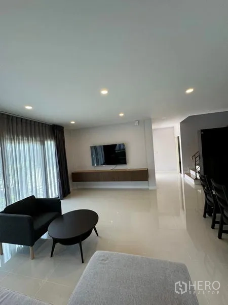 Detached House for rent in Don Mueang, Bangkok - Spacious living area with wall-mounted TV console, floor-to-ceiling curtains and recessed ceiling lights.