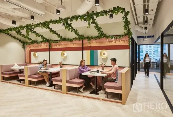 办公空间 出租在Pathum Wan, Bangkok - 现代办公室内的彩色卡座区，绿植吊顶与壁灯装饰。