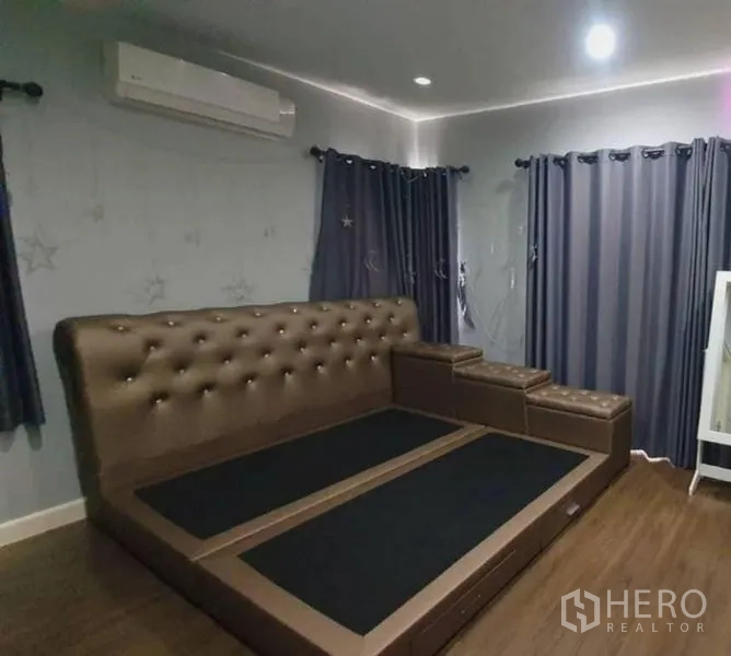 Detached House for sale in Pathum Thani - Cozy bedroom featuring a tufted bed frame, dark curtains and wood floors.