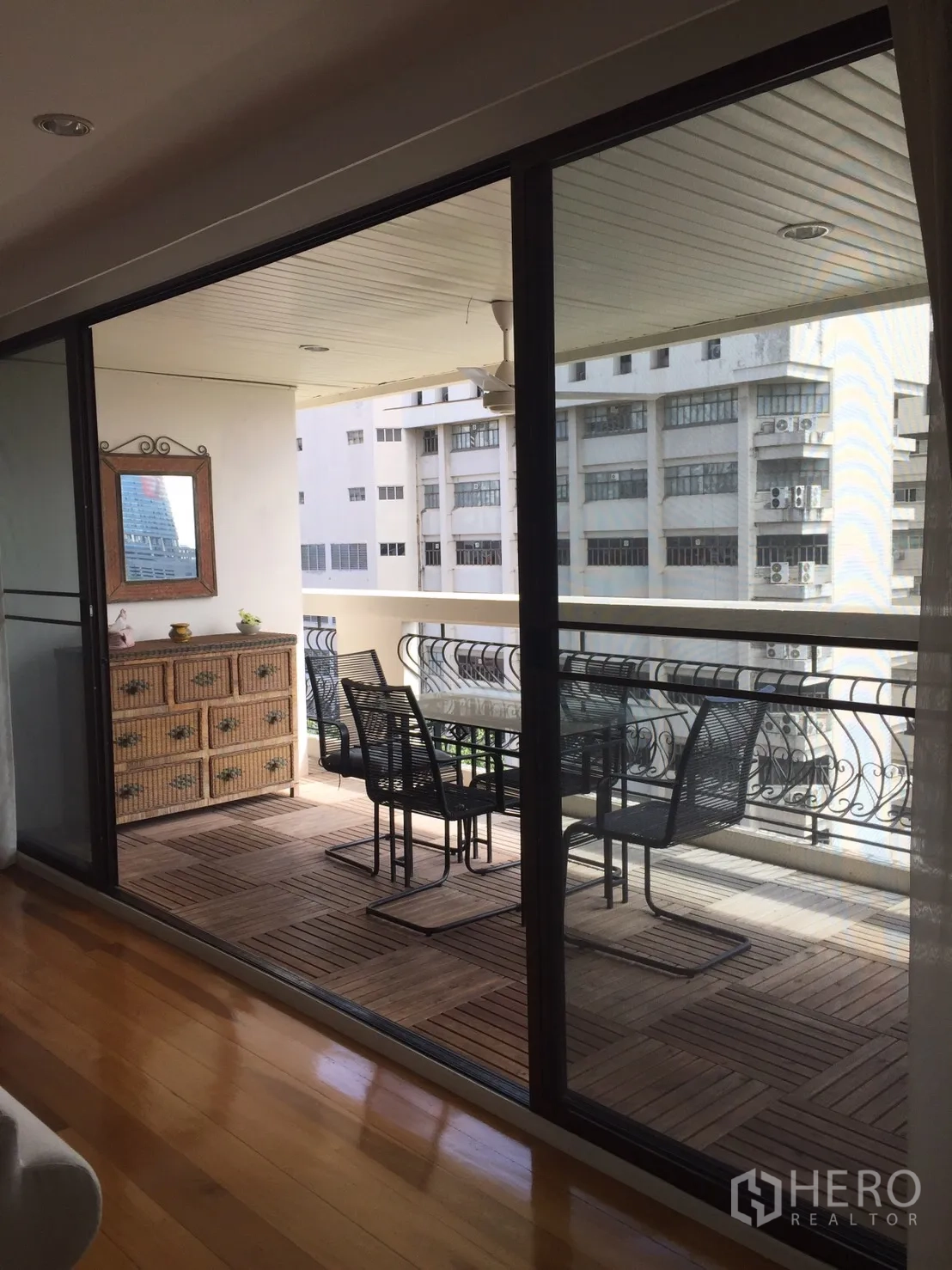 Condominium for rent in Watthana, Bangkok - Covered balcony with wood decking, sliding glass doors and dining set overlooking neighboring buildings.