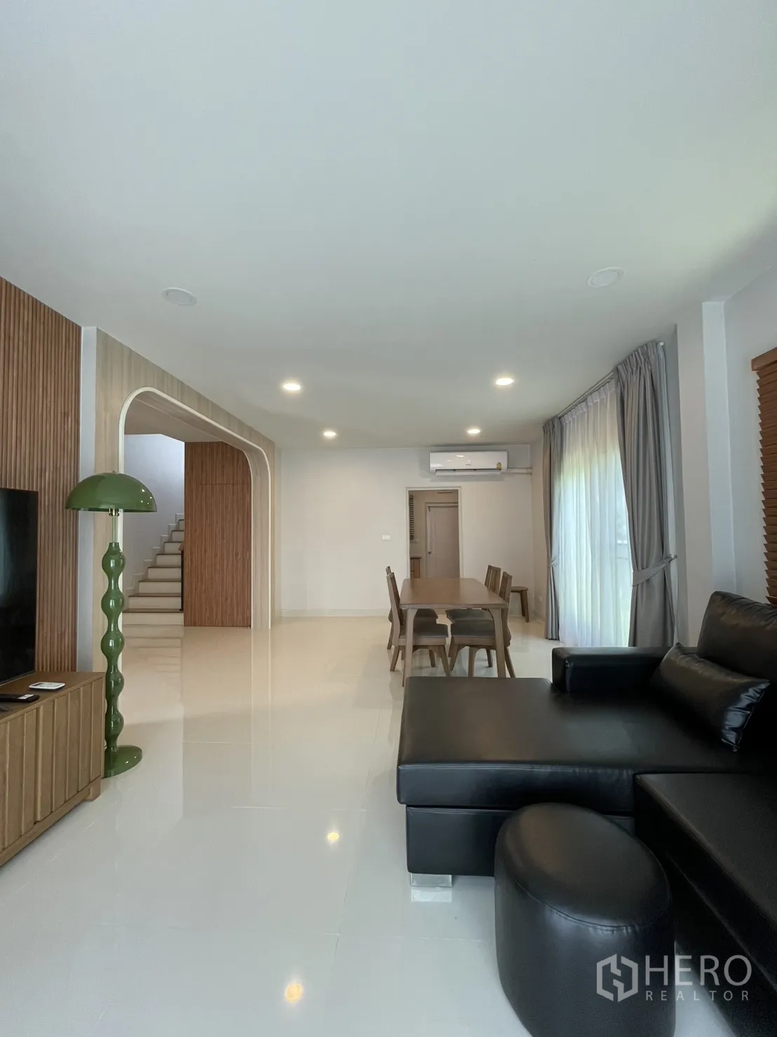 Detached House for rent in Bang Phli, Samut Prakan - Open-plan living and dining area with black leather sectional, wooden dining table and bright curtains.