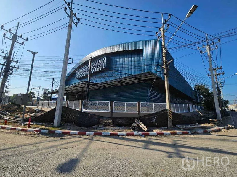 工厂 出租在Chon Buri - 蓝色金属外墙厂房转角外观，带围栏与电线杆