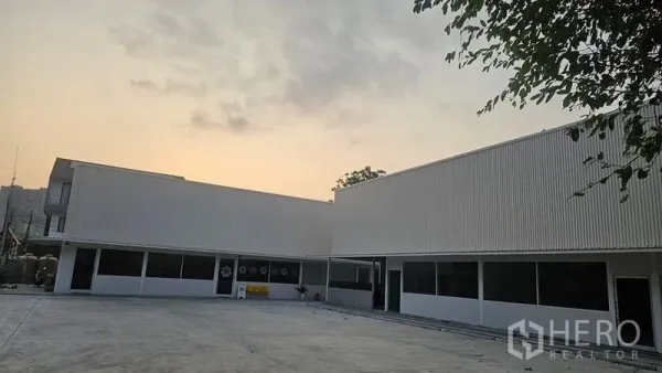 สำนักงาน ให้เช่าในBang Phli, Samut Prakan - อาคารสำนักงานโลว์ไรส์สีขาว ผนังเมทัลชีท หน้าต่างบานยาว และลานคอนกรีตกว้างยามพระอาทิตย์ตก