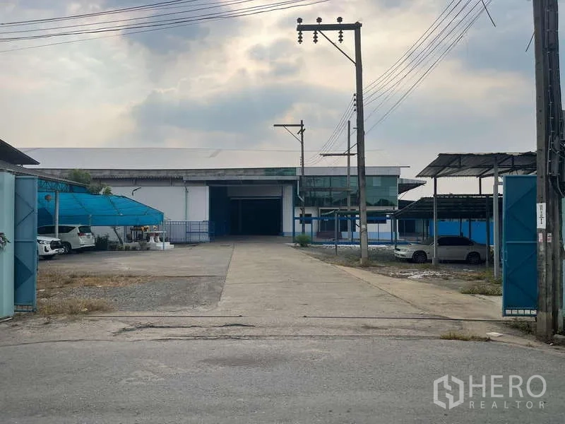 Warehouse for rent in Nong Khaem, Bangkok - Street-side view of a gated industrial property with parking shelters and wide access.