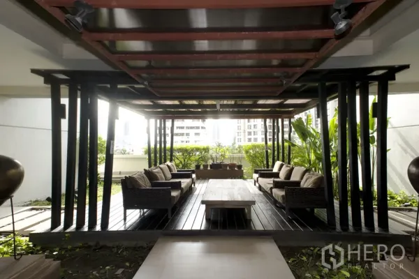 Condominium for rent in Sathon, Bangkok - Shaded outdoor lounge pavilion with wooden deck, rattan sofas and greenery at a Sathon condominium.