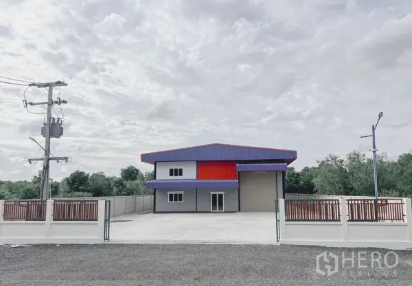 货栈 出租或出售在Khlong Luang, Pathum Thani - 现代仓库正面，带大门与宽阔混凝土前院及两层办公区，周围绿树。