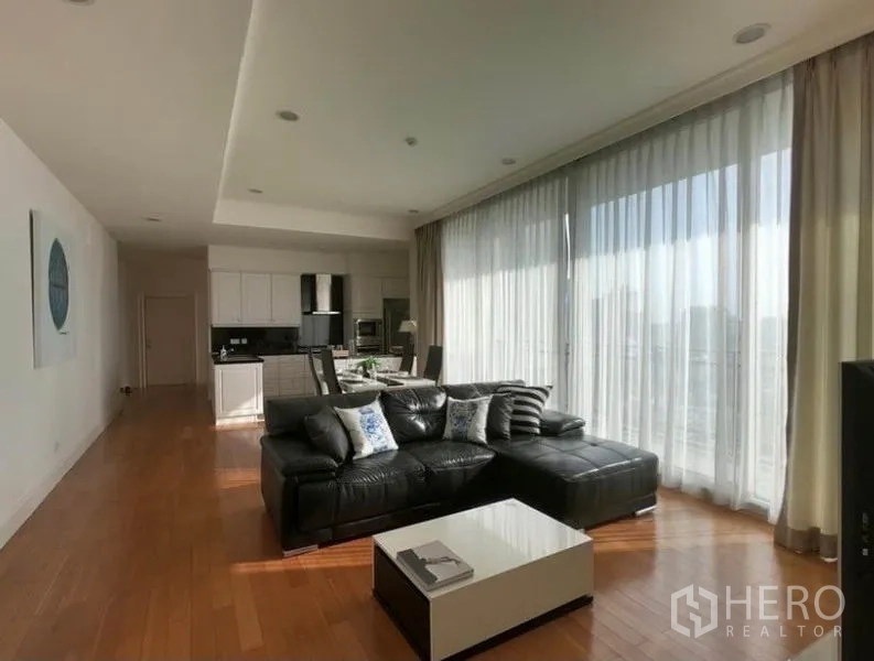 Condominium for rent in Watthana, Bangkok - Bright open-plan living room with black leather sectional, sheer floor-to-ceiling curtains and city view.