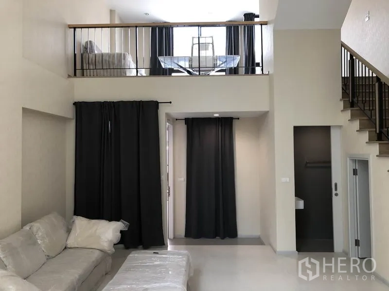 Townhouse for rent in Suan Luang, Bangkok - Living room with mezzanine loft above, staircase and blackout curtains.