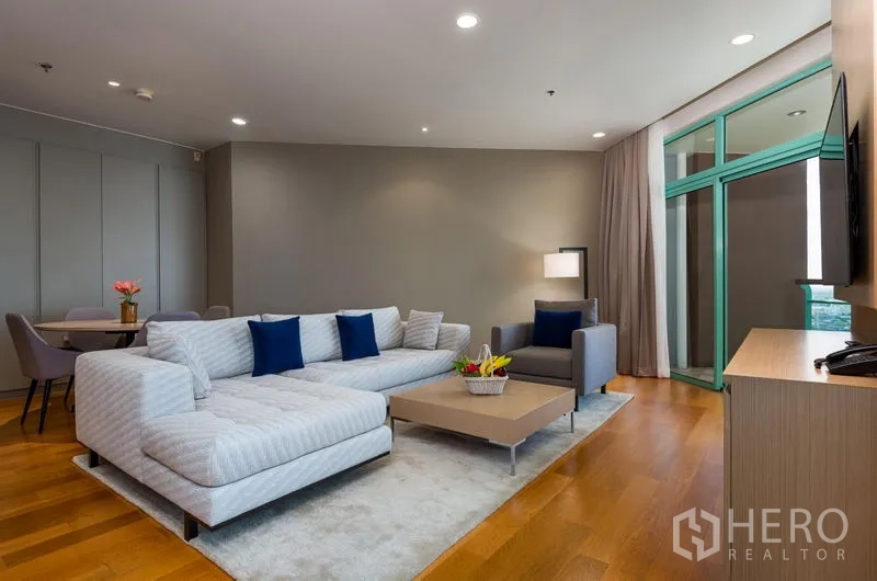 Condominium for rent in Bang Kho Laem, Bangkok - Contemporary living room with sectional sofa, TV wall and balcony-height glass doors.