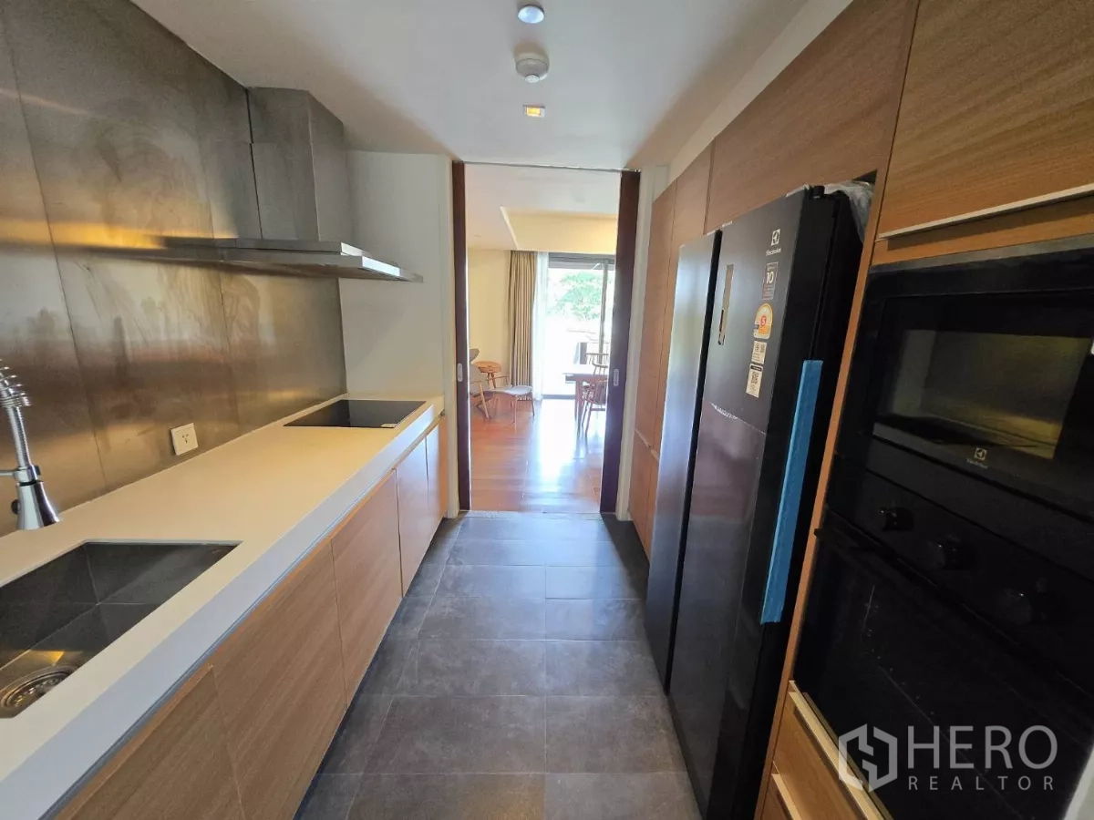 公寓 出租在Yan Nawa, Bangkok - 现代长廊式厨房，电磁炉、嵌入式烤箱与冰箱，望向餐区。