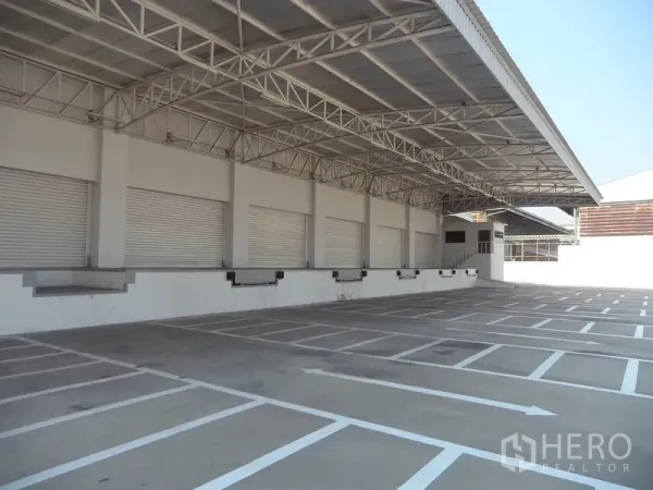Warehouse for rent in Bang Sao Thong, Samut Prakan - Wide truck court with marked bays facing a row of loading docks under a roof.