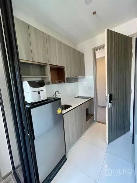 公寓 出租在Watthana, Bangkok - KnightBridge Prime On Nut 厨房，木质柜体、冰箱与白色防溅板的紧凑型走道式布局。