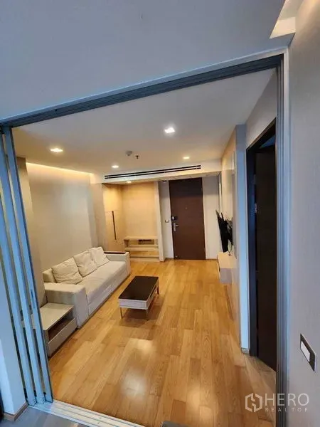 Condominium for sale in Ratchathewi, Bangkok - Cozy living room with sofa, wall-mounted TV, coffee table and recessed lighting on wood floors.