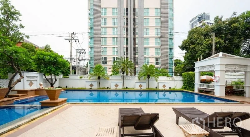 Condominium for sale in Watthana, Bangkok - Outdoor swimming pool with sun loungers, greenery and a low-rise condominium building.