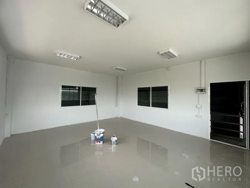 Factory for rent in Pathum Thani - Bright tiled office room with fluorescent lighting and windows overlooking factory floor.
