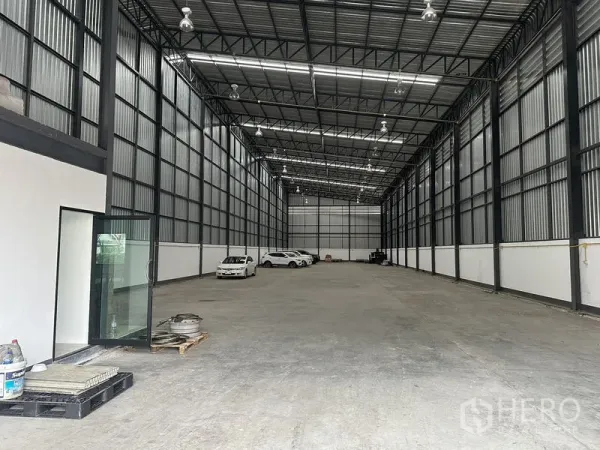 货栈 出租在Samut Prakan - 通长无柱仓库地面，金属墙面，尽头停放有车辆。