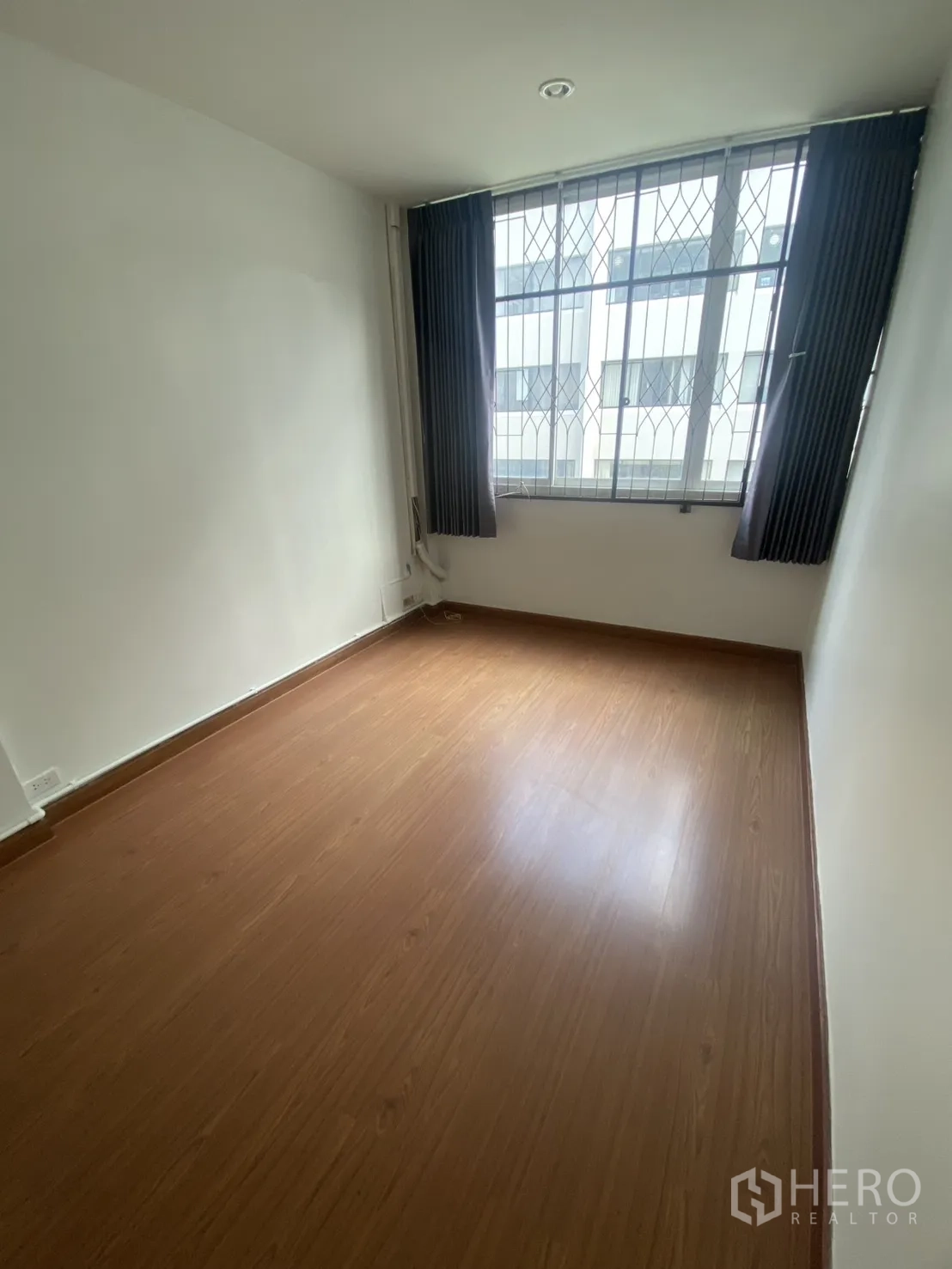 Shophouse for rent in Bang Rak, Bangkok - Bright room with large barred window, curtains, and wood-look floor.