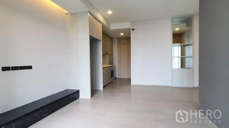 Condominium for sale in Khlong Toei, Bangkok - Bright open-plan living area with light wood floors, built-in TV ledge and kitchenette in a modern condo.