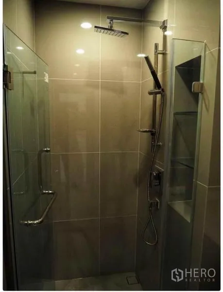 Condominium for rent in Huai Khwang, Bangkok - Bathroom with glass-enclosed rain shower and handheld shower set.