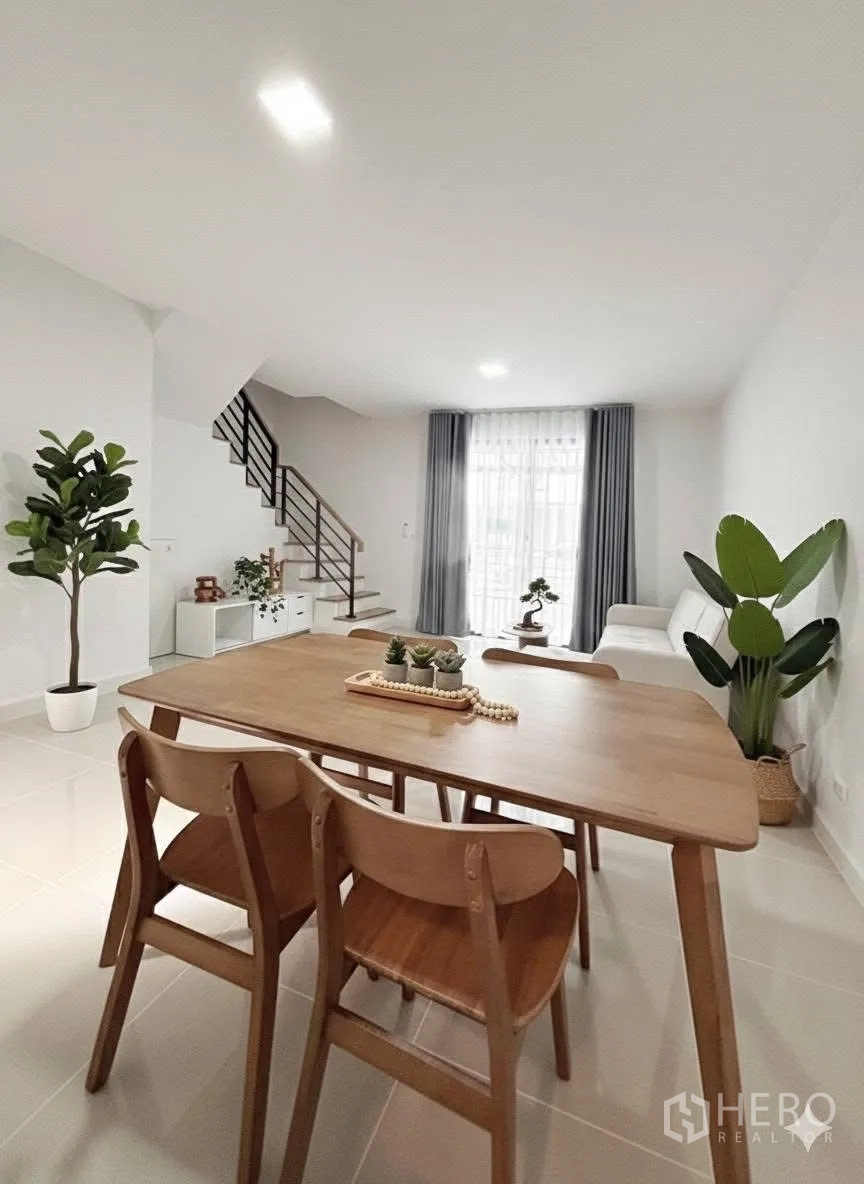 联排别墅 for rent in Bang Phli, Samut Prakan - 餐区视角，木质餐桌与室内绿植，通向客厅与楼梯