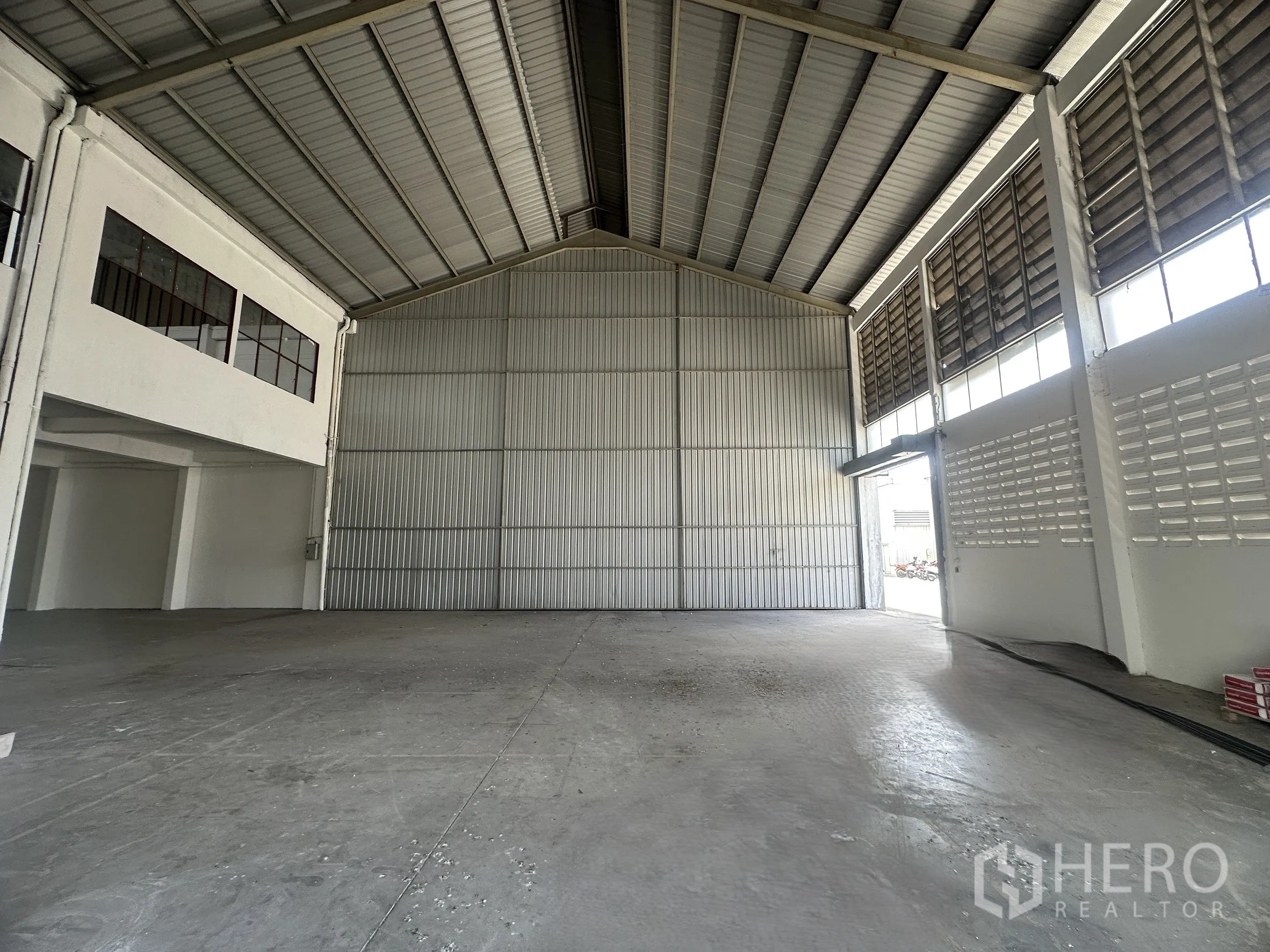Factory for rent in Mueang Samut Prakan, Samut Prakan - Spacious factory interior with high steel roof, concrete floor, and tall sliding door for loading.