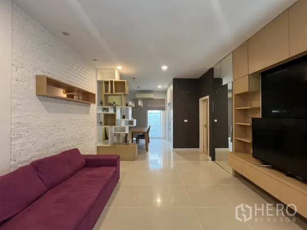 Townhouse for rent in Wang Thonglang, Bangkok - Open-plan living room with purple sofa, built-in TV wall and shelving.