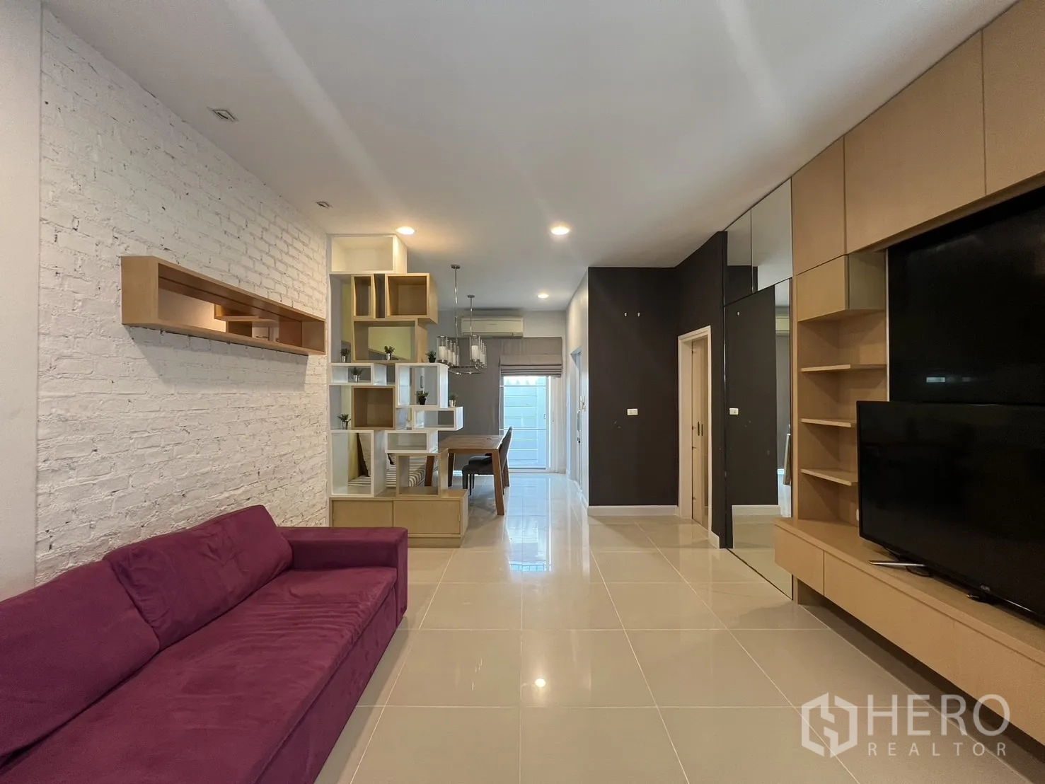 Townhouse for rent in Wang Thonglang, Bangkok - Open-plan living room with purple sofa, built-in TV wall and shelving.