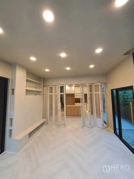 Detached House for sale in Prawet, Bangkok - Bright living area with recessed lights, herringbone floor, and folding glass doors opening to the kitchen.