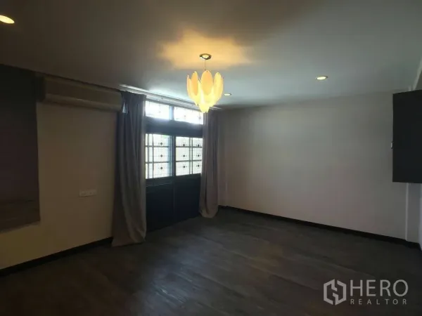 Townhouse for rent in Khlong Toei, Bangkok - Bedroom with dark wood flooring, air-conditioning unit, large window with curtains, and modern pendant light.
