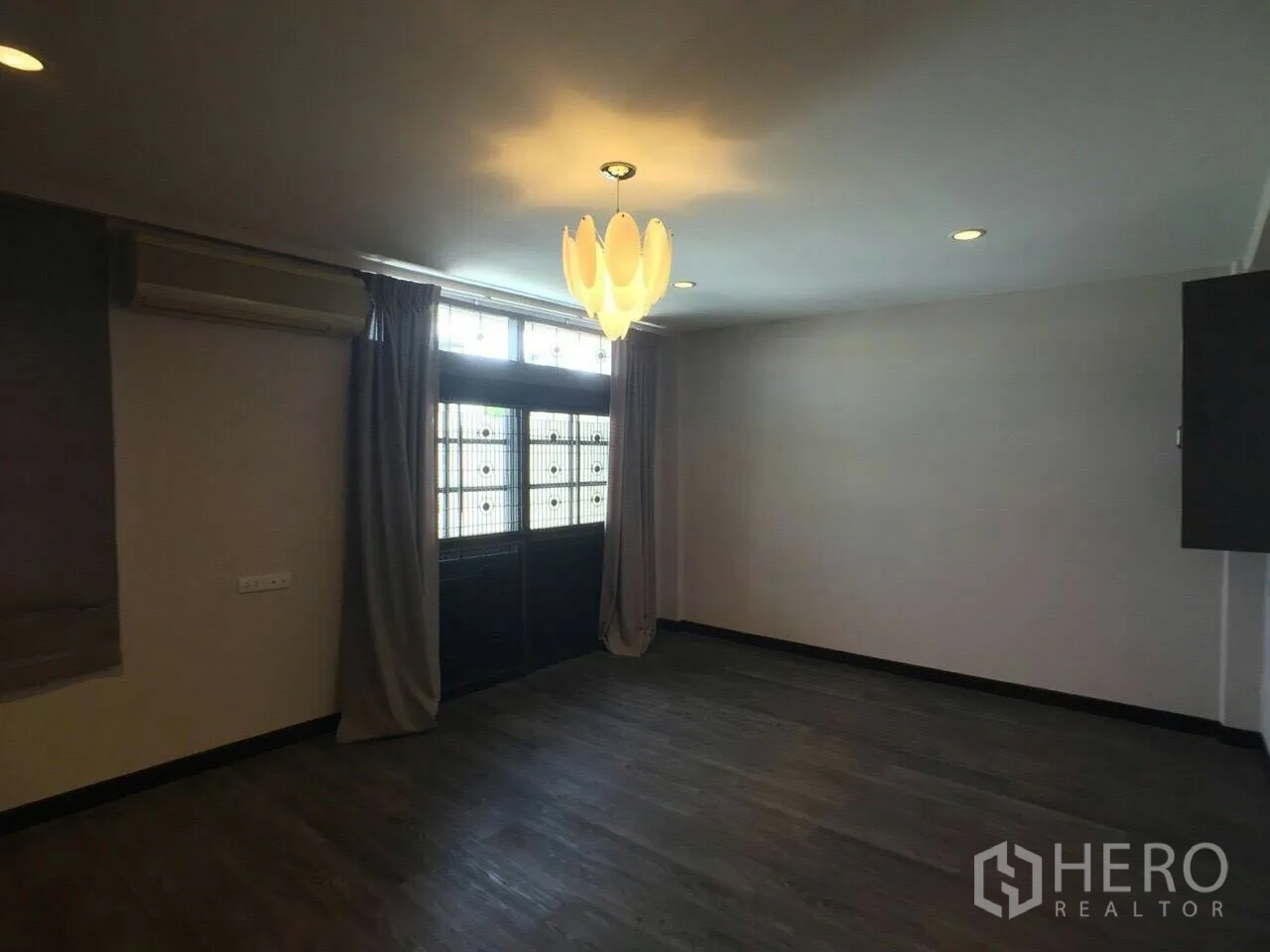 Townhouse for rent in Khlong Toei, Bangkok - Bedroom with dark wood flooring, air-conditioning unit, large window with curtains, and modern pendant light.