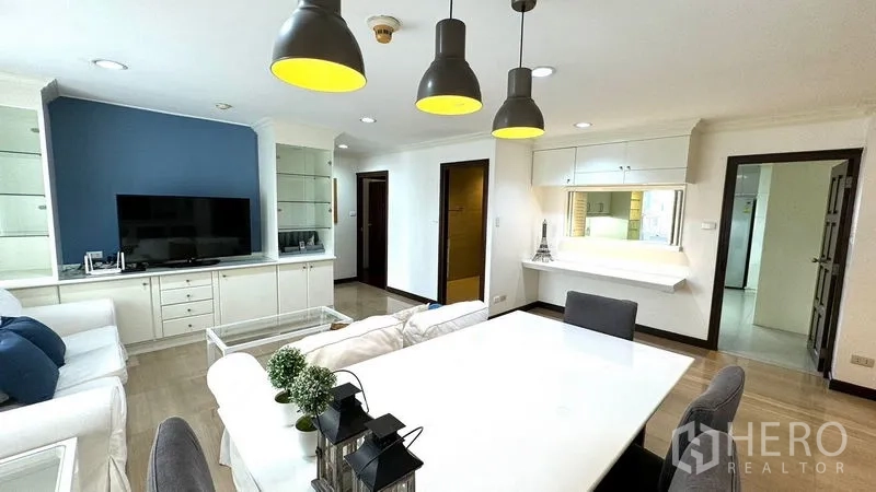 คอนโด ให้เช่าหรือขายในWatthana, Bangkok - พื้นที่นั่งเล่นและรับประทานอาหารแบบโอเพนพร้อมโซฟาสีขาว ผนังทีวี และโคมไฟแขวนโทนดำ